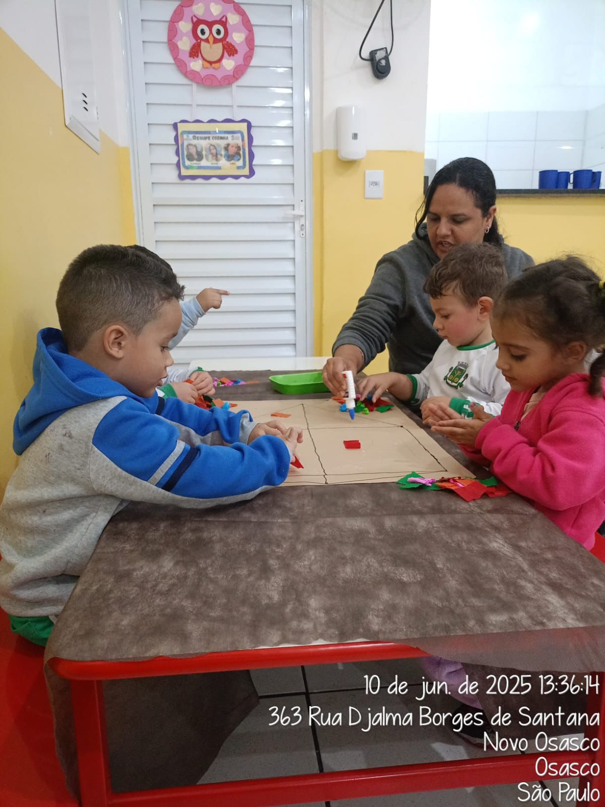 Educadora auxiliando crianças em atividade de colagem na mesa